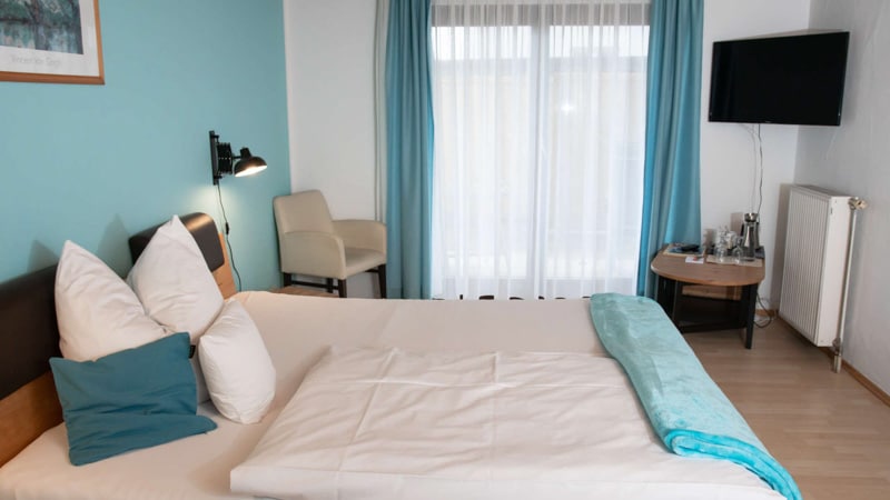 Helles Doppelzimmer im Hotel Garni Möwe Tutzing mit Massivholzmöbeln, türkisfarbenen Akzenten, Balkonzugang und Flachbildschirm-TV